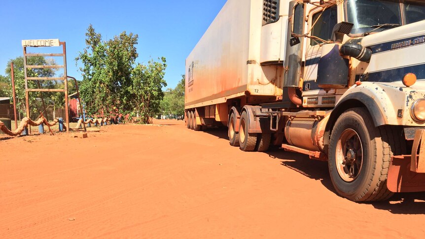 A large truck on red dirt in a remote community delivers goods