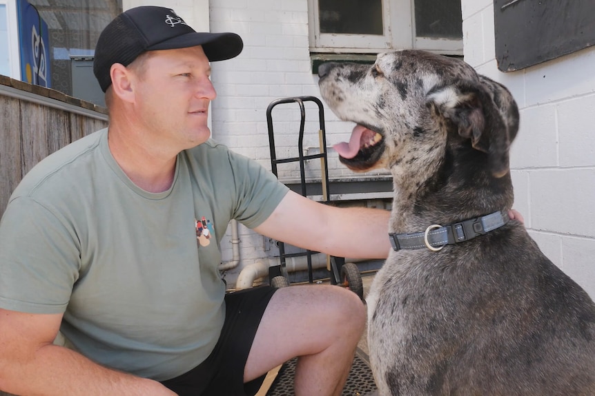 A man and his Great Dane dog get close and smile face-to face outside a pub.