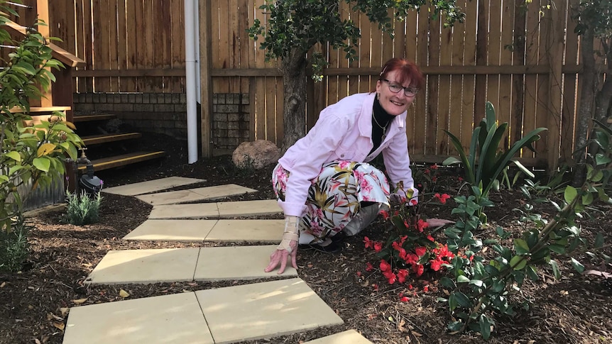 A woman crouches near flowers in a garden.
