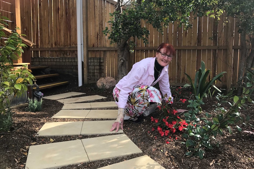 A woman crouches near flowers in a garden.