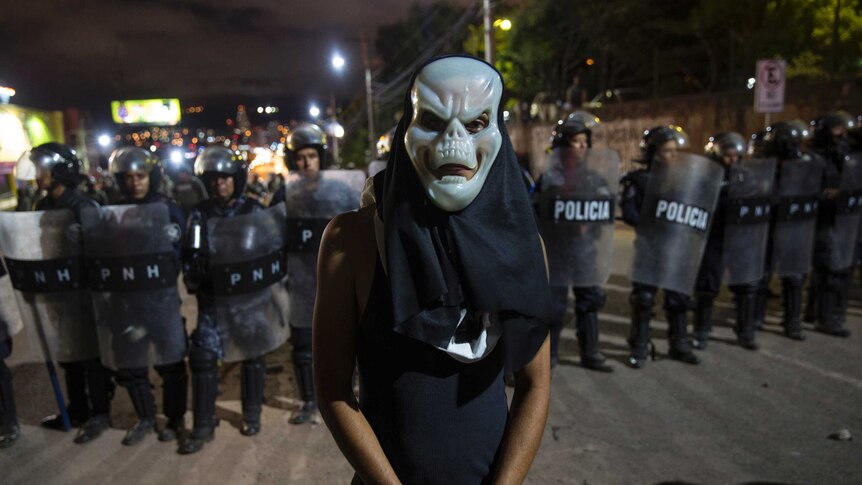 A man wearing a mask stands in front of a police barricade.