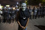 A man wearing a mask stands in front of a police barricade.
