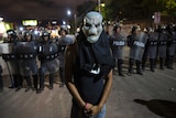 A man wearing a mask stands in front of a police barricade.