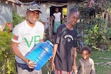 A smiling Vanuatuan man in a white T-shirt, holding a large water container, beside an older woman in blue t-shirt and child.