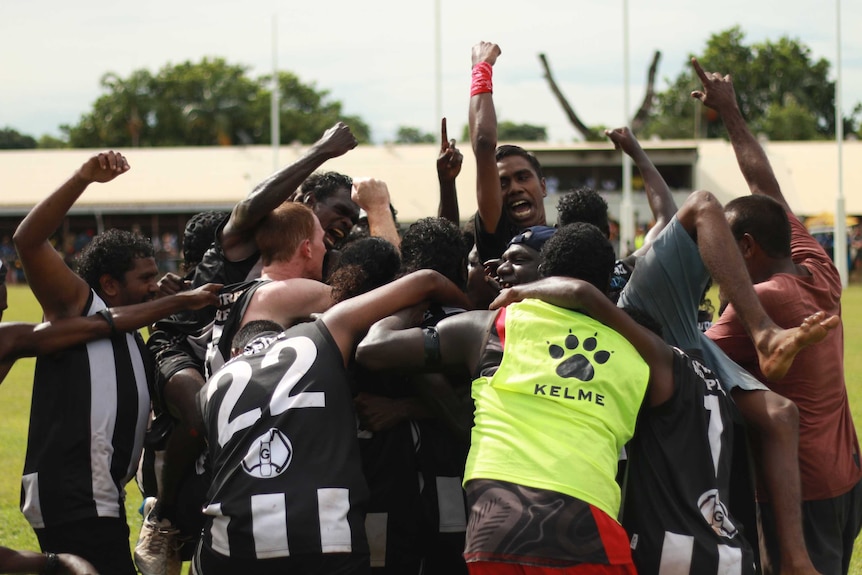 Players from the Muluwurri Magpies celebrate in a huddle together after winning the Tiwi football grand final.