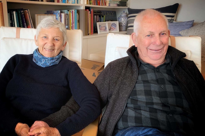 Pam and Neil Thorne sit in comfortable chairs, side by side, holding hands.