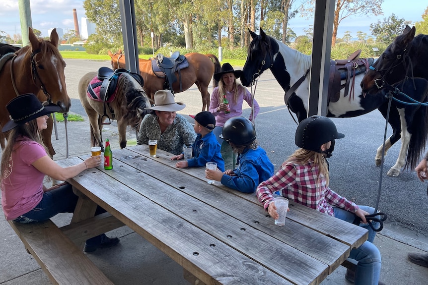 Riders enjoy a beer at the Toora pub with horses in background.