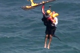 A man being winched from the ocean into a helicopter, tethered to a paramedic.