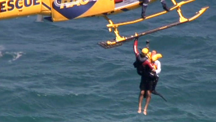 A man being winched from the ocean into a helicopter, tethered to a paramedic.