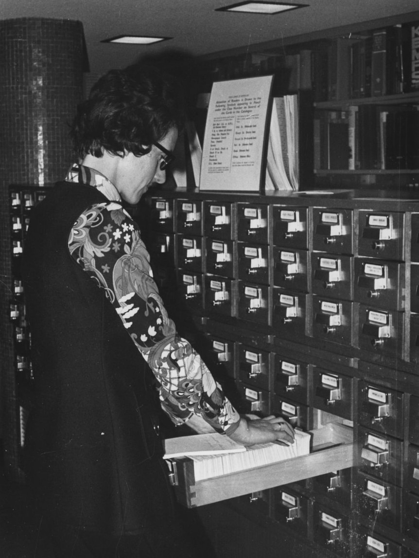 A lady looks through the card catalogues in a library.