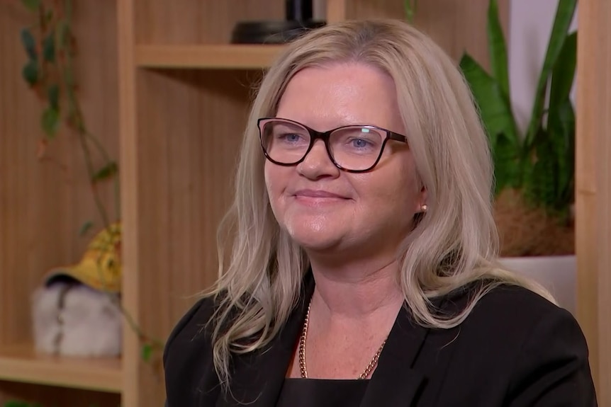 Woman in office in black jacket wearing glasses.