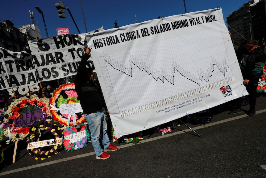 Two people holding a large banner showing a graph with a downward trend