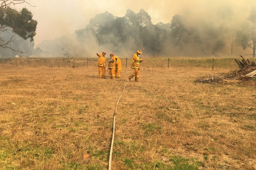 Four men in orange suits with smoke billowing behind them.