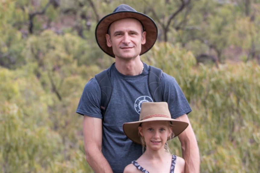 A man in a hat stand with a young girl in the bush smiling