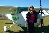 Catherine Fitzsimmons stands at the front of a small plane with her arm leaning on its propeller.