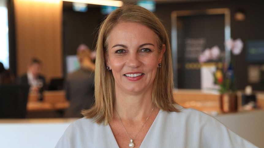 Jo Masters stands in an office wearing a white top.