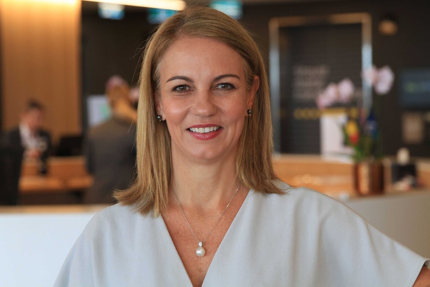 Jo Masters stands in an office wearing a white top.