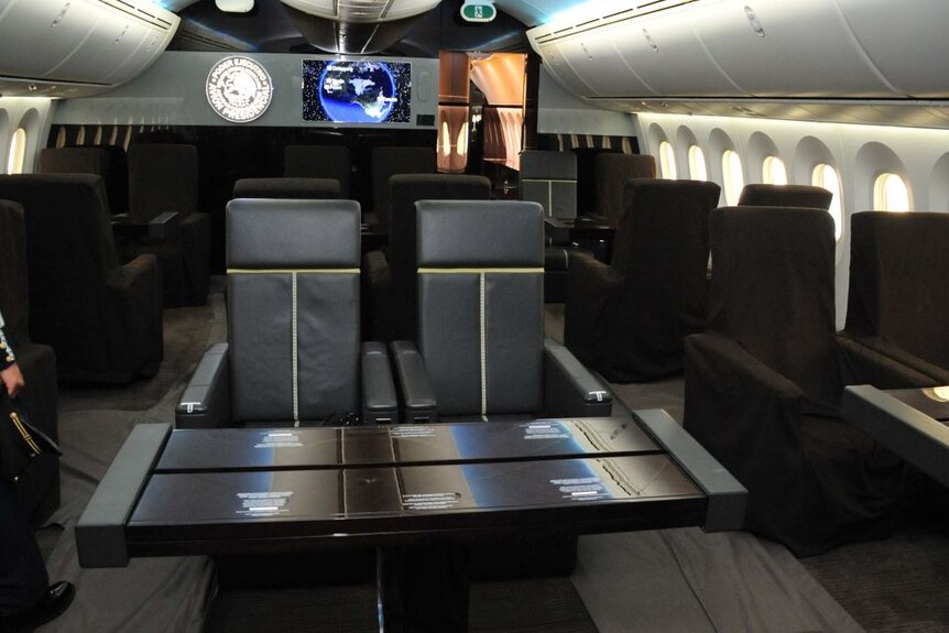 Brown leather seats with tables in front of them spaced through the interior of a plane