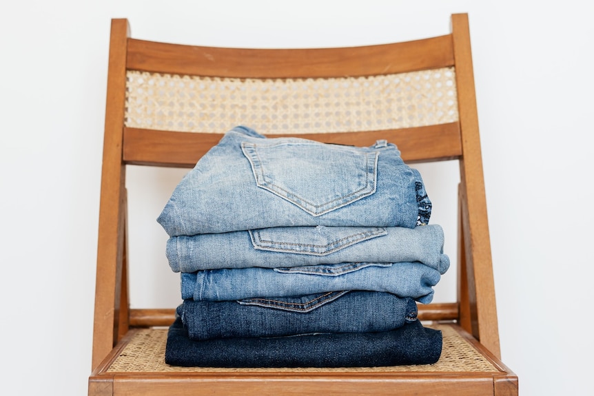 A pile of folded pairs of jeans on a chair