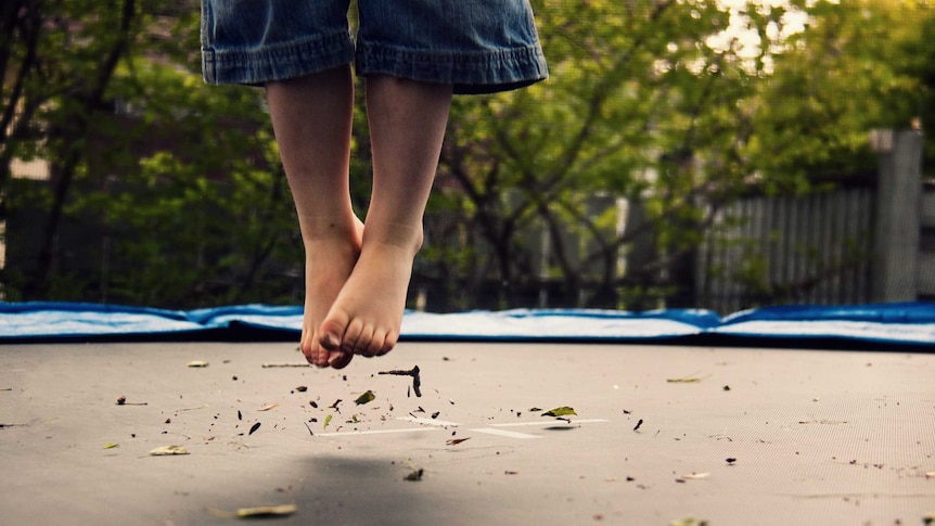 A child's feet and lower legs in the air above a trampoline surface.