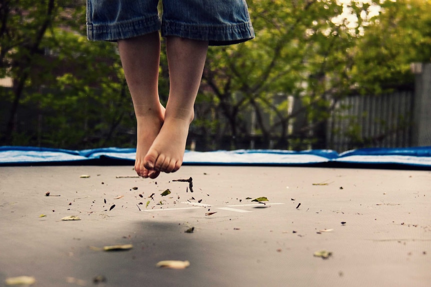 A child's feet and lower legs in the air above a trampoline surface.
