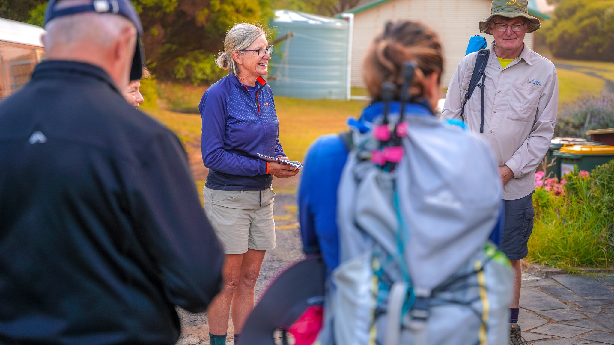 A woman wearing hiking gear and glasses stands in a circle of walkers smiling.