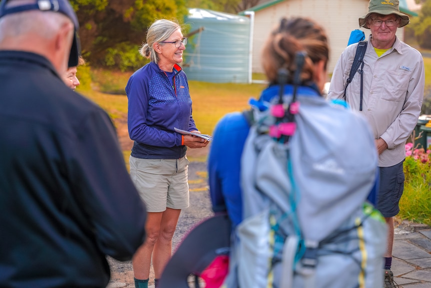 A woman wearing hiking gear and glasses stands in a circle of walkers smiling.
