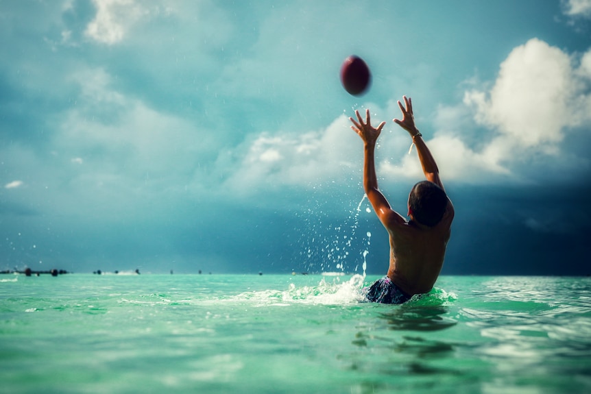A man falls backward in the water to catch a ball on a cloudy day.