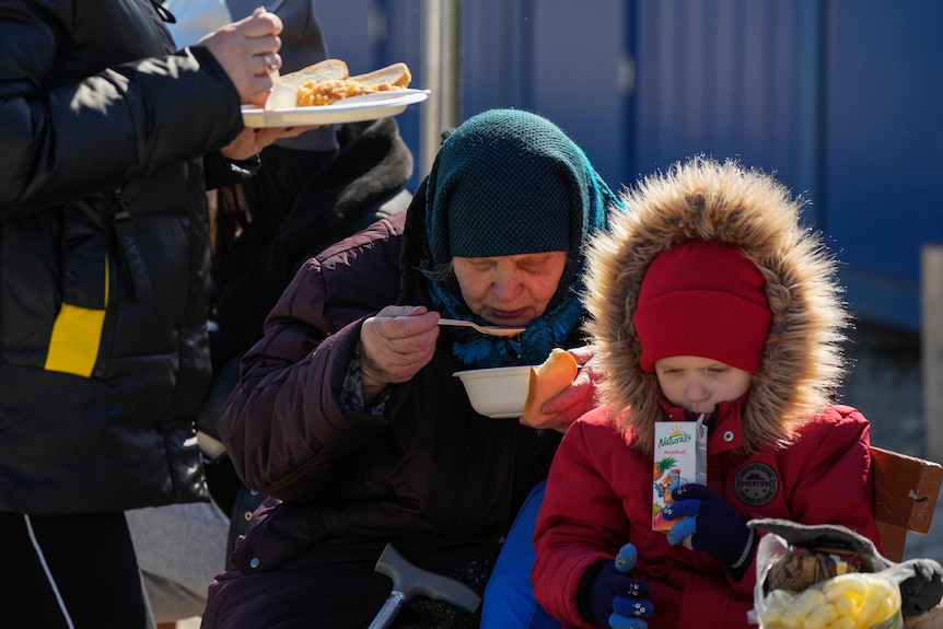 A woman and child in warm clothing eat a meal using disposable plates and cutlery.