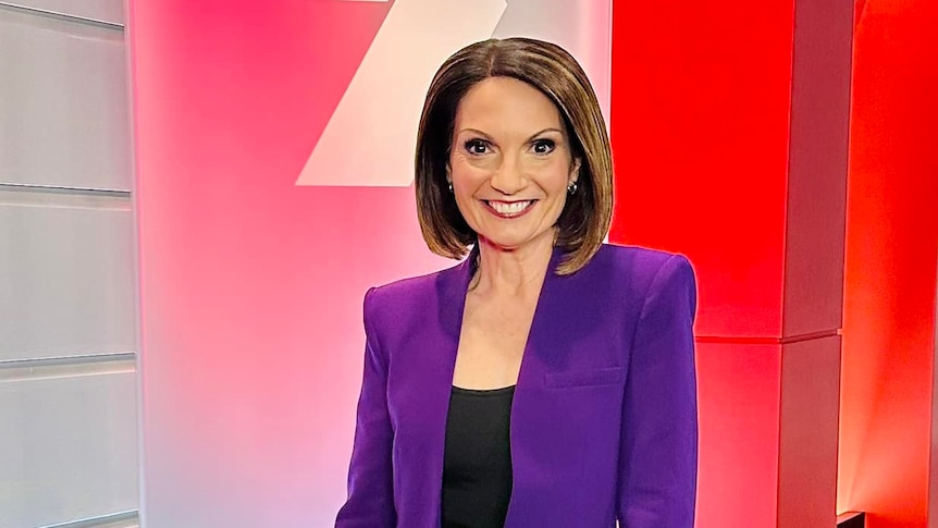 A woman in a purple suit smiling standing in front of a 7 News sign