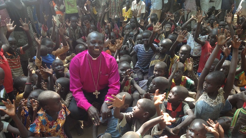 A bishop kneels down to talk with a group of children