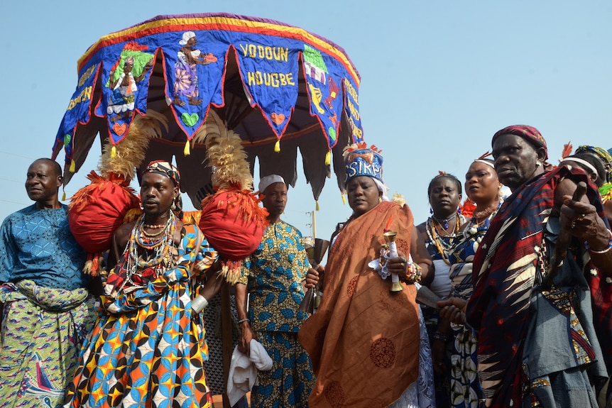 A group of people in colourful clothing with a large umbrella