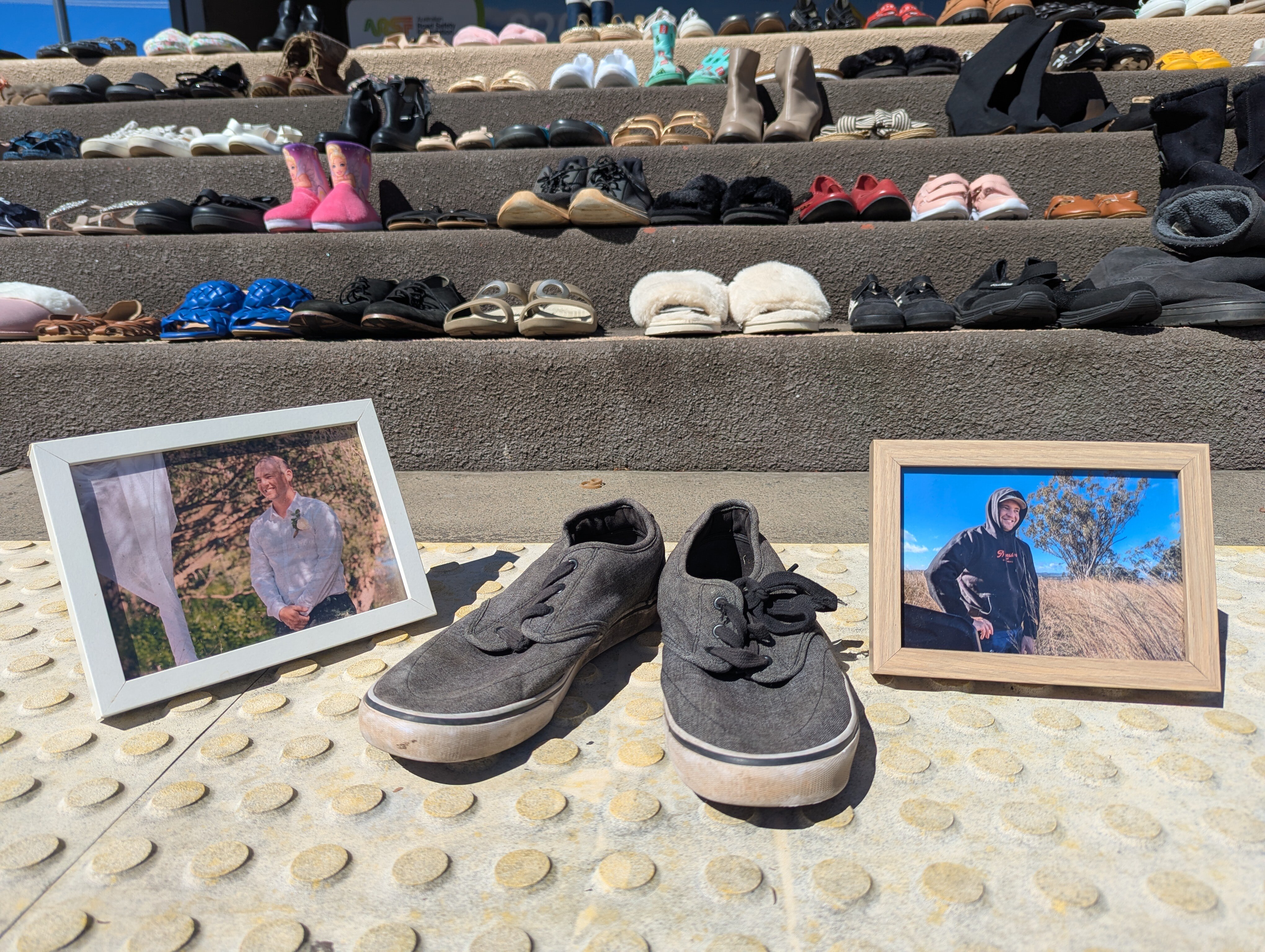 A pair of black men&#x27;s shoes between two framed photos of a young man, with rows of shoes on steps in the background.