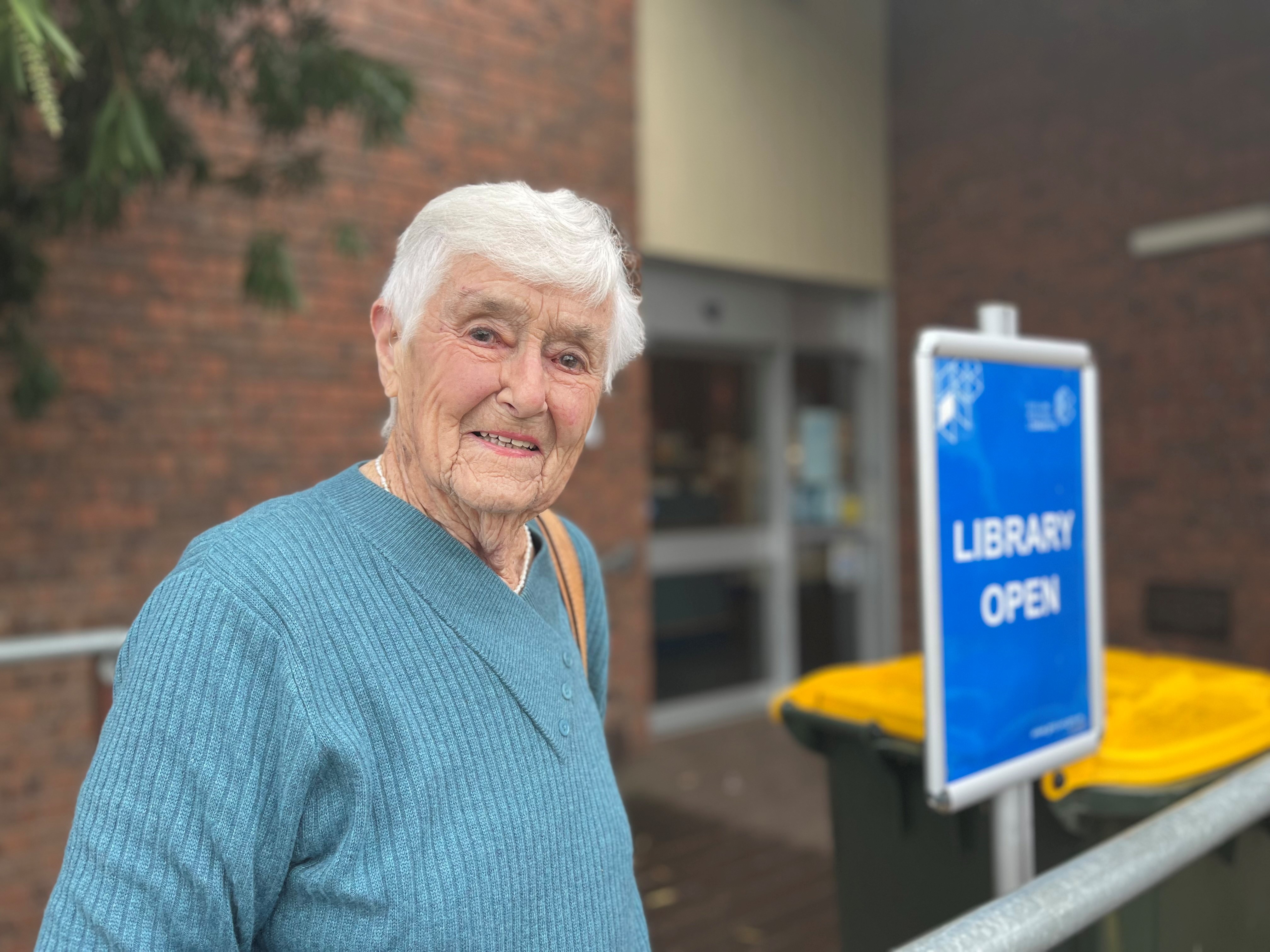 Betty smiles as she stands in front of a library building.