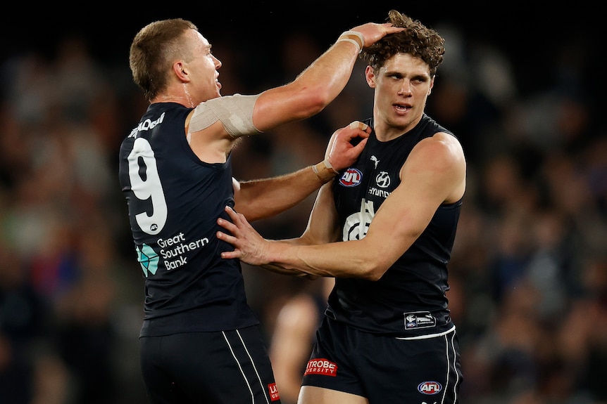 A Carlton AFL player congratulates a teammate after he kicked a goal.