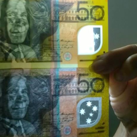 Two $50 notes held up one below the other, with the bottom one allegedly counterfeit.