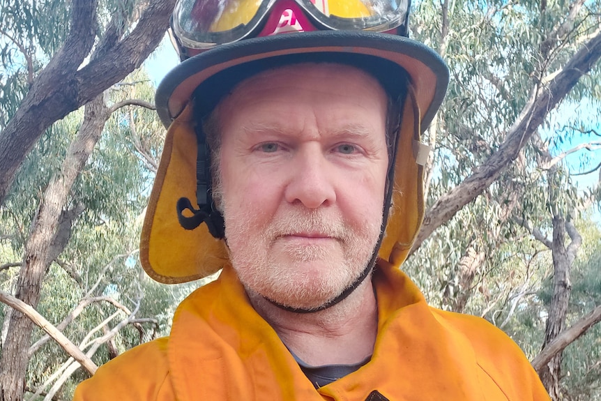 A man in a bright orange CFA uniform and helmet, with white stubble, looking at the camera.