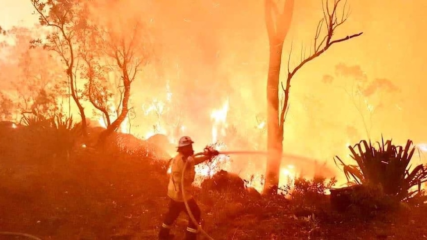 firefighter hosing an intense bushfire