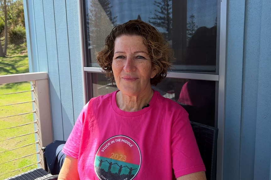 A woman in pink top sits outside a caravan