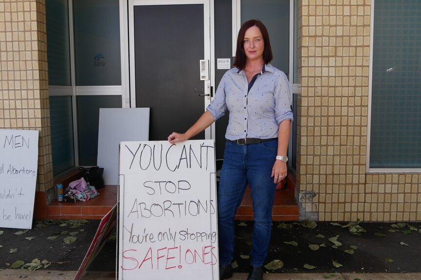 A woman stands on a street holding a placard.