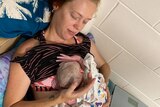 a woman lays propped up by pillows cradling a new born baby after childbirth