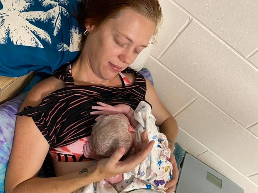 a woman lays propped up by pillows cradling a new born baby after childbirth