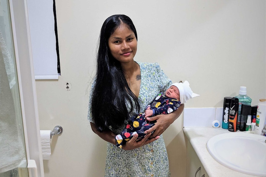 A woman standing in an ensuite holding a newborn.