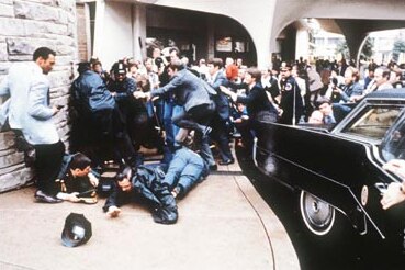 三名男性倒在地上，周围是人群，旁边是一辆黑色的美国总统座车。