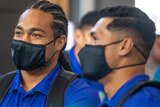 Two New Zealand Warriors NRL players stand next to each other with their arms folded wearing masks and backpacks