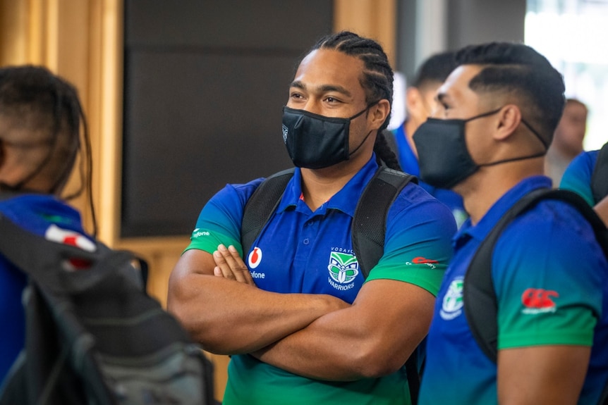 Two New Zealand Warriors NRL players stand next to each other with their arms folded wearing masks and backpacks