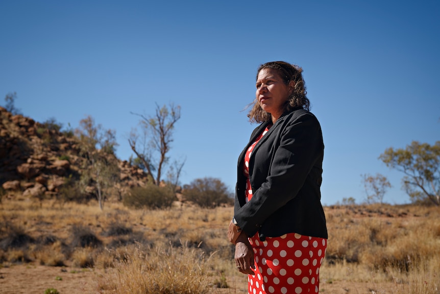 A serious-looking woman looking out into the distance against a desert backdrop.