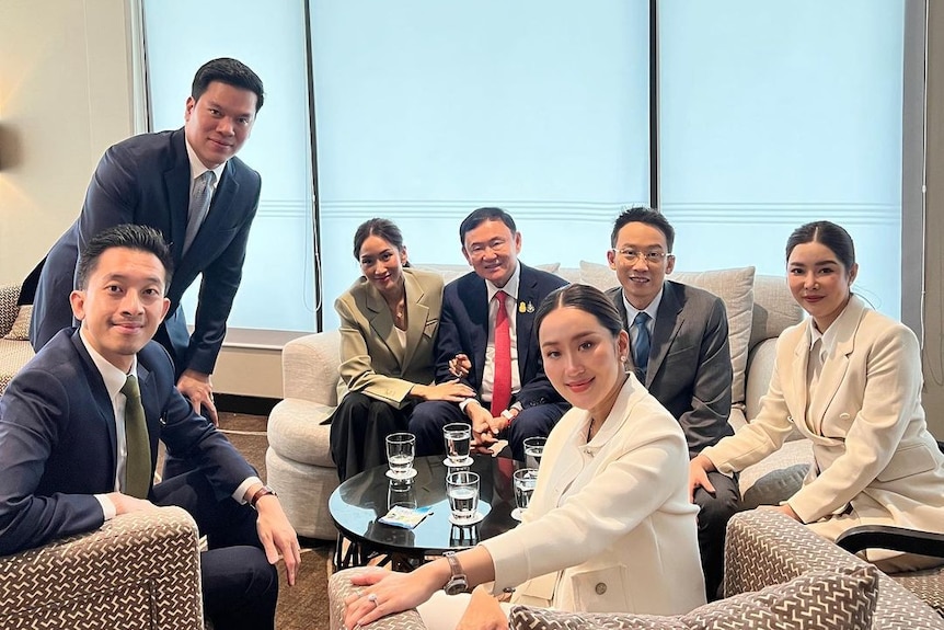 A group of people in suits sit around a coffee table 