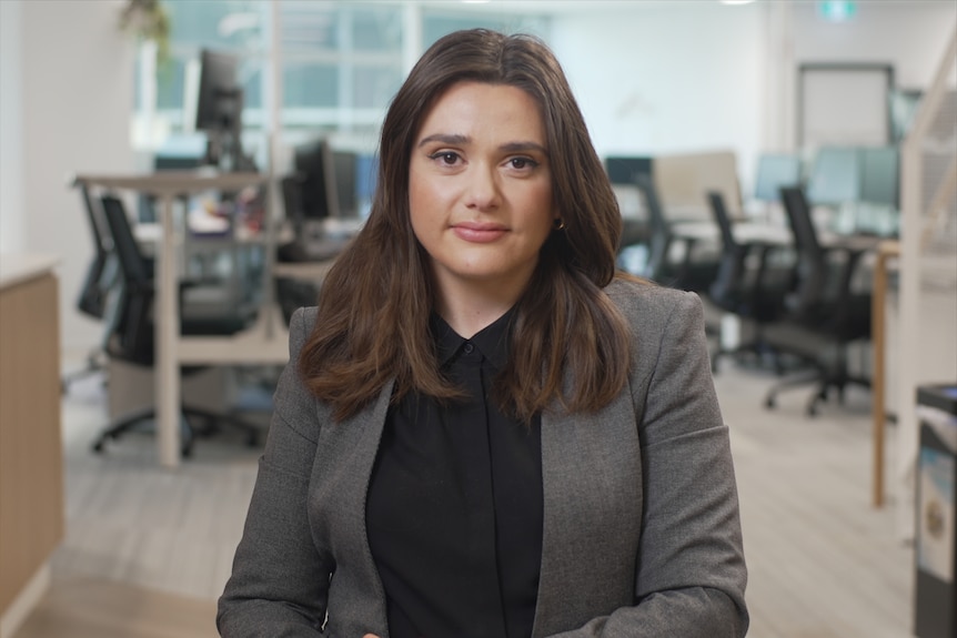 A young, formally dressed woman with long, dark hair sits in an office.