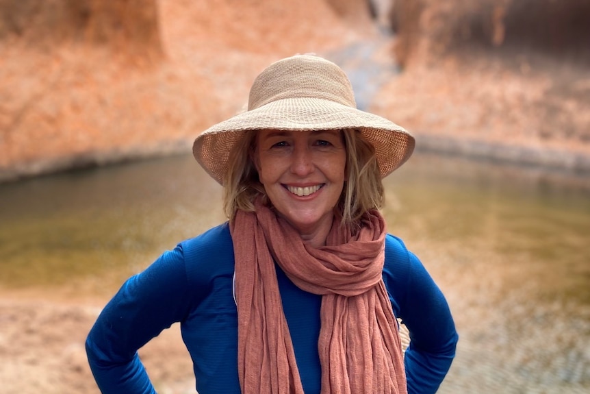 A portrait of Andrea Gilbert smiling and wearing a hat in an outdoor setting